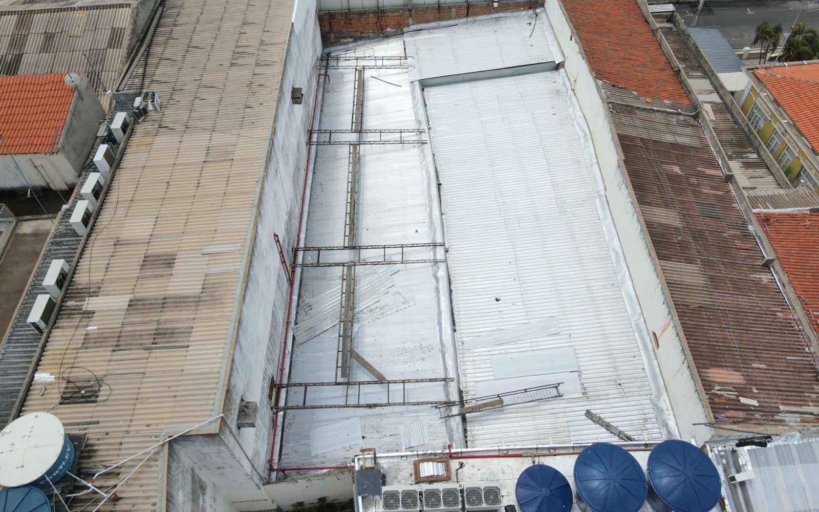 Foto de drone de cobertura metálica de prédio comercial com telhas soltas e estrutura exposta.