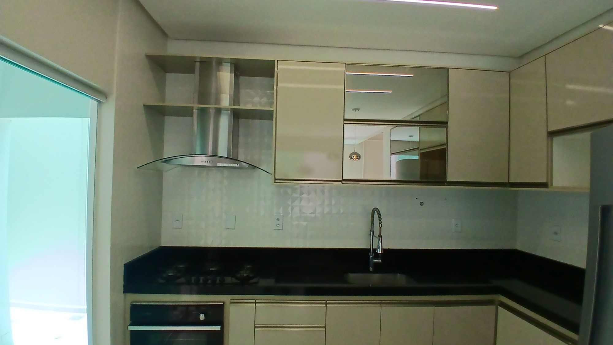 Cozinha planejada com bancada de granito preto, coifa de inox e armários claros.
