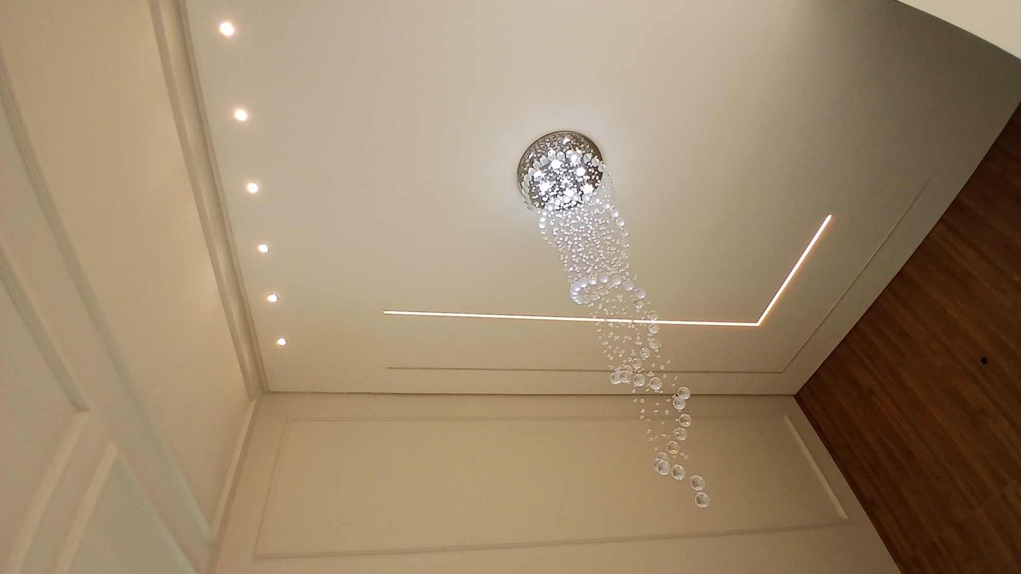 Teto da sala de pé-direito duplo com lustre de cristal, spots embutidos e fita de LED.