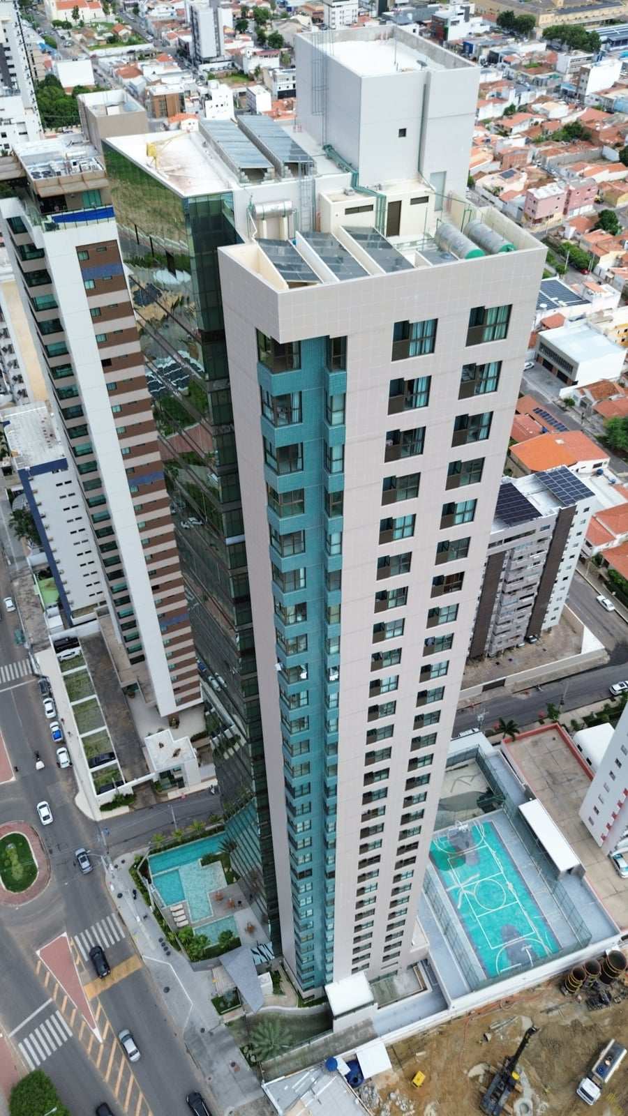 Foto de drone de um prédio residencial alto, vista de cima, com a área de lazer ao pé da torre.
