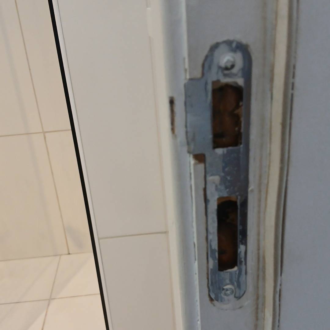 Entrada: chapa da fechadura no batente da porta, com a pintura gasta em volta, fotografada do mesmo ponto.