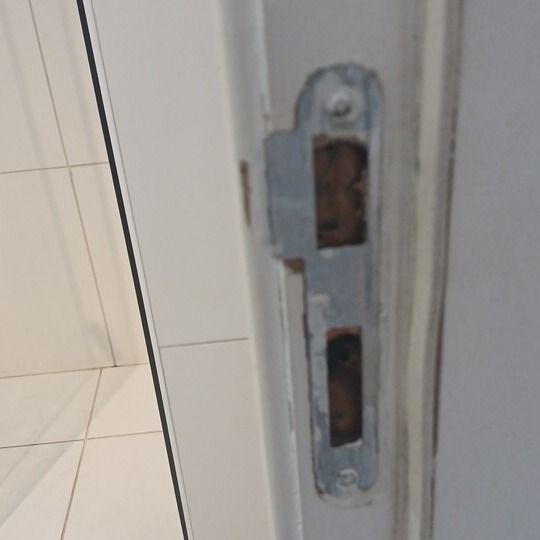 Saída: chapa da fechadura no batente da porta, com a pintura gasta em volta, fotografada do mesmo ponto.