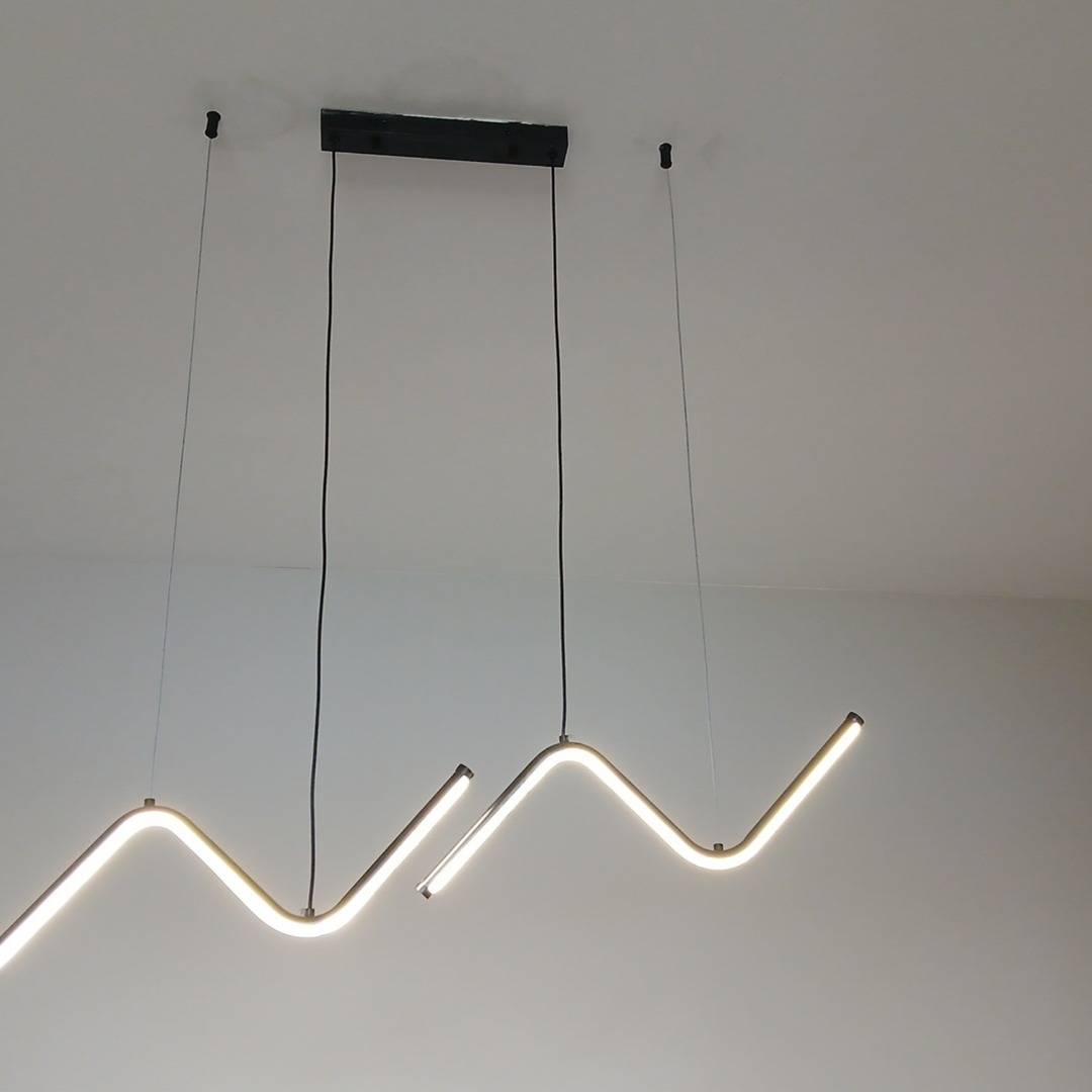 Entrada: luminária pendente em zigue-zague acesa no teto da sala, fotografada do mesmo ponto.