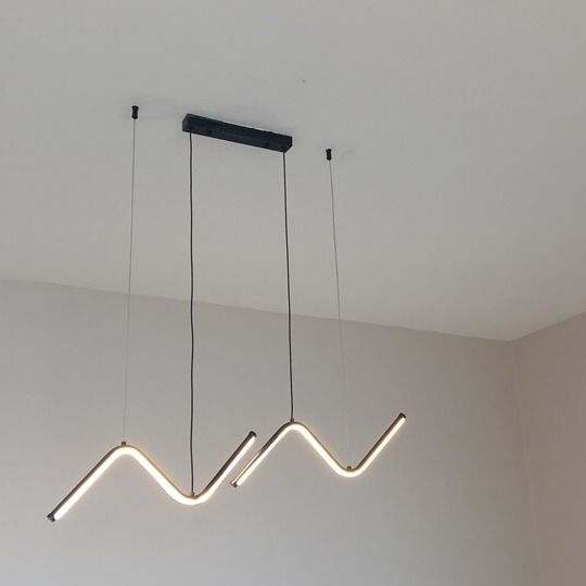 Saída: luminária pendente em zigue-zague acesa no teto da sala, fotografada do mesmo ponto.