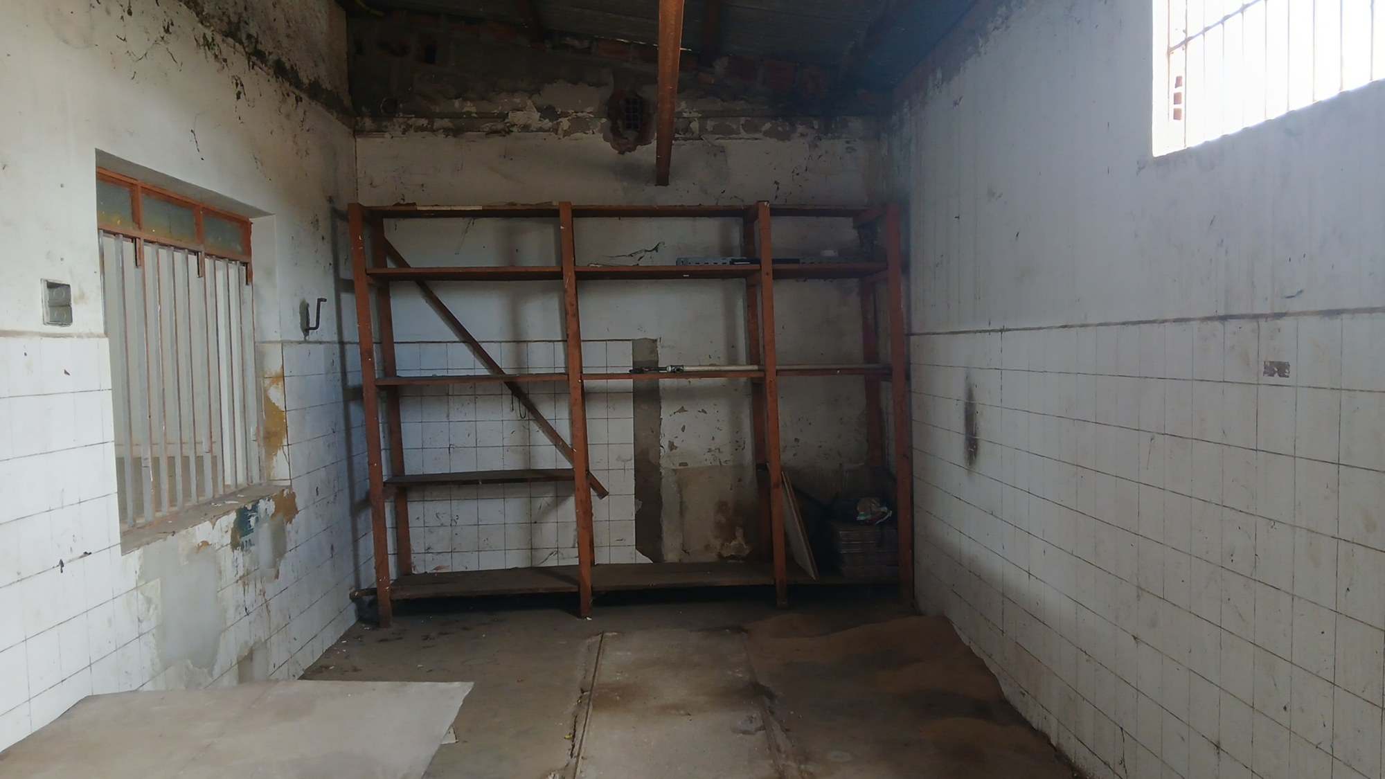 Parede de depósito com azulejos brancos, manchas de umidade e reboco aparente.