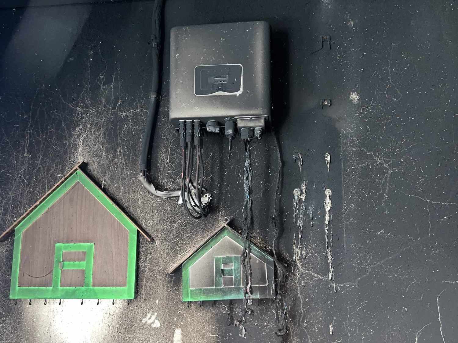 Parede escurecida pelo fogo, com uma caixa elétrica no alto, fiação derretida e o quadro de disjuntores embaixo.