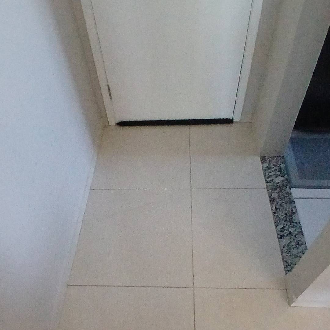 Entrada: piso cerâmico claro da sala diante de uma porta branca, fotografado do mesmo ponto.