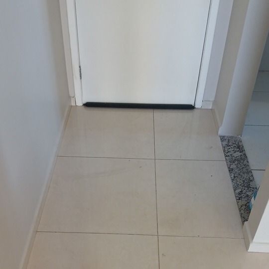 Saída: piso cerâmico claro da sala diante de uma porta branca, fotografado do mesmo ponto.