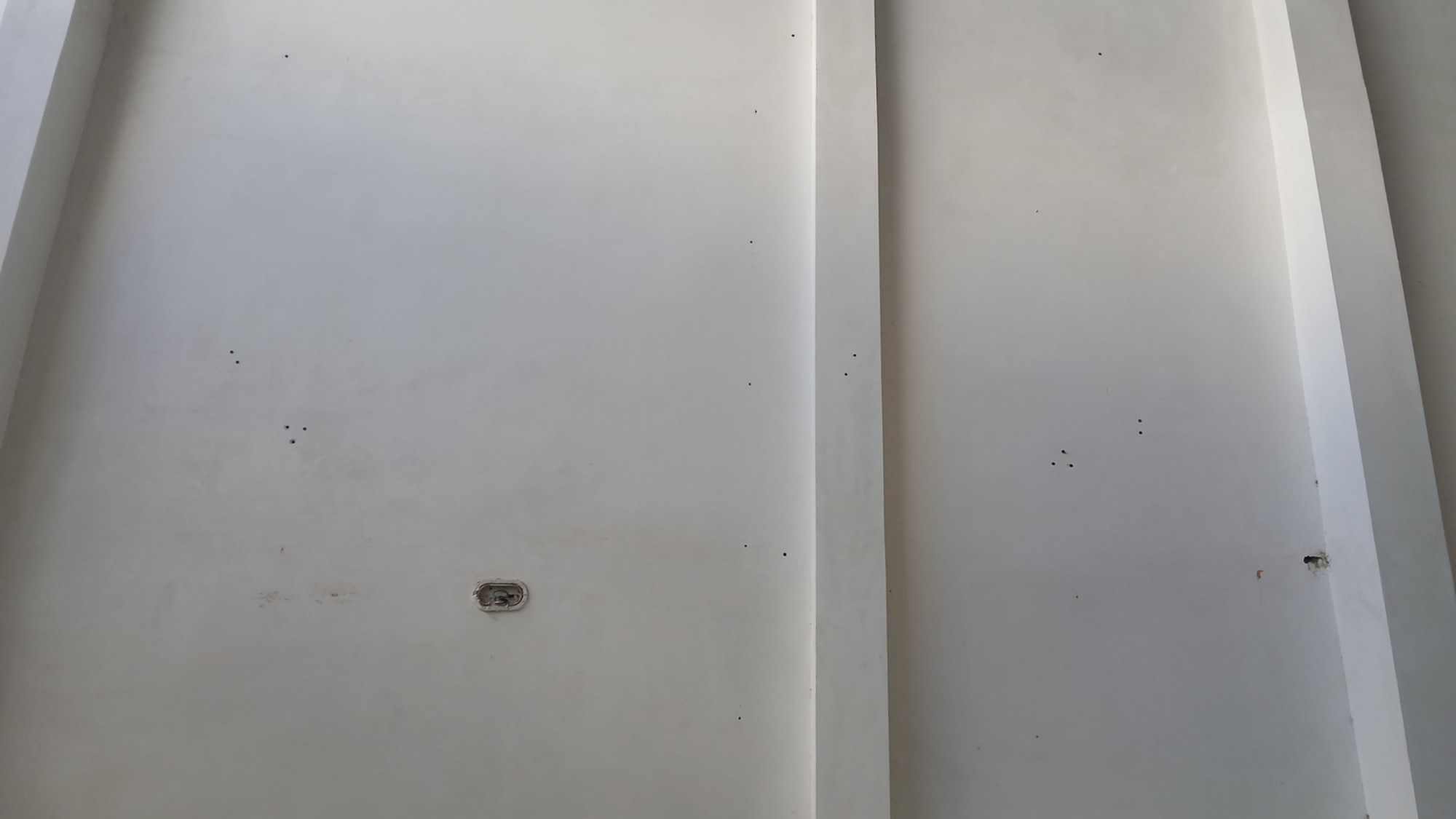 Parede clara do galpão com furos, buchas e marcas registrados antes da reforma.