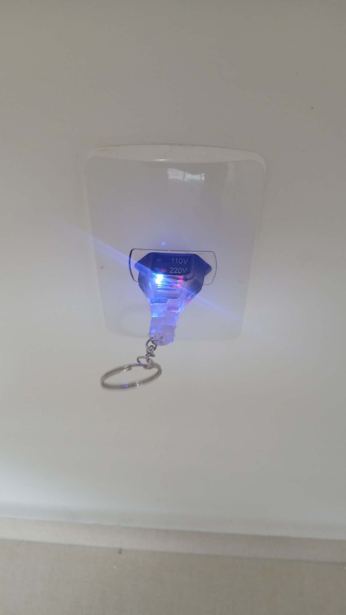 Tomada branca com testador encaixado e luz azul acesa.